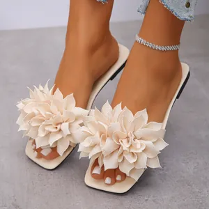 Close-up detail of stylish beige square toe flat slides with large chiffon flower decoration.