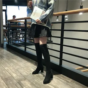 Bottes cuissardes noires à talons hauts stylées avec une jupe et un pull.