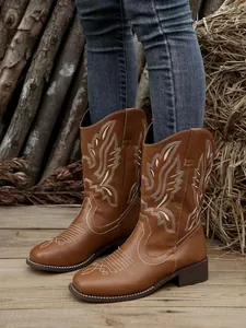 Detail shot of brown Western cowboy boots with white embroidery worn with denim jeans outdoors