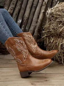 Women's brown western cowboy boots with white ethnic embroidery in rustic setting