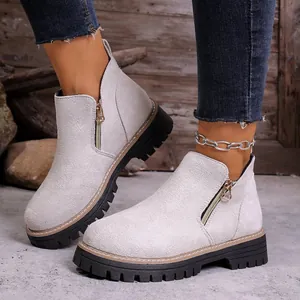 Detail view of light grey suede ankle boots with side zippers and chunky black soles.