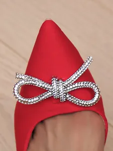 Gros plan d'élégants escarpins rouges à bout pointu avec un nœud en strass étincelant.