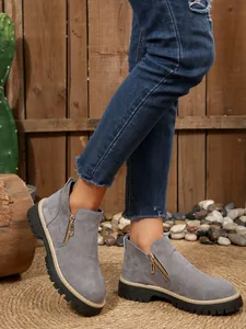Side-profile view of grey suede ankle boots with side zipper worn with blue jeans