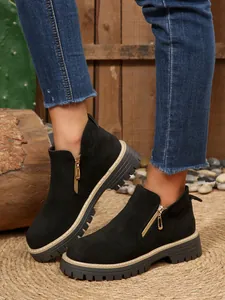 Detailed view of black suede ankle boots with gold side zippers and chunky lug soles