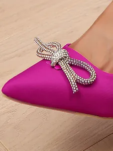 Vue rapprochée d'élégants escarpins en satin fuchsia avec un nœud en cristaux étincelants.