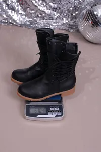 Detail view of a black faux leather mid-calf knight boot being weighed on a digital scale