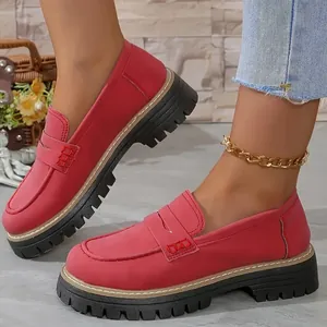 Gros plan de mocassins rouges mats à semelles épaisses crantées sur les pieds d'un modèle.