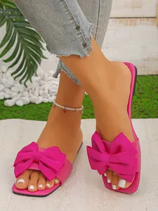 Close-up detail of bright pink flat sandals with a large decorative fabric bow