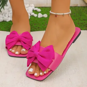 Close-up of bright pink women's flat sandals featuring a large fabric bow