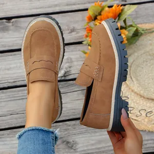 Détail de mocassins en daim marron avec semelles compensées noires sur fond en bois