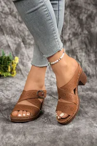 Close-up view of brown hollow-out high-heeled sandals with buckle strap worn by a model