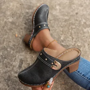 Detailed view of vintage black carved mules featuring chunky heels and decorative gold buckle