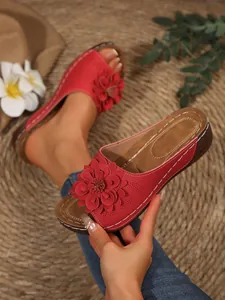 Close-up of red wedge sandals with large floral detail and white stitching