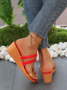 Primo piano di eleganti ciabatte con zeppa rosse e oro indossate con jeans blu