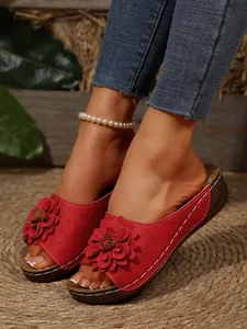 Detail of women's red wedge sandals featuring a large 3D flower and white stitching.