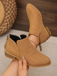 Detailed view of tan pointed toe ankle boots featuring back zipper with fringe tassel