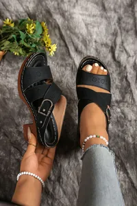 Close-up of black chunky heel sandals with cutout patterns and decorative metal buckles