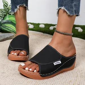 Detail shot of black wedge platform sandals with contrast stitching on a textured rug