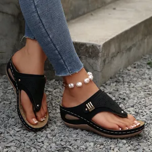Detail of black wedge flip-flop sandals with laser-cut patterns and white stitching