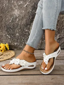 Detailed view of white wedge thong sandals with 3D floral accents and rhinestones