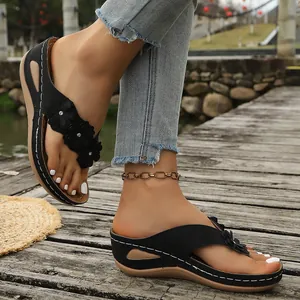 Primer plano de chanclas con cuña negras con elegantes detalles floraux en terraza de madera.