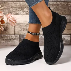 Primo piano di sneaker slip-on in maglia nera traspirante su modella con sfondo rustico
