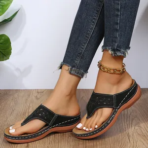 Detalle en primer plano de sandalias de cuña negras con diseño calado y costuras blancas
