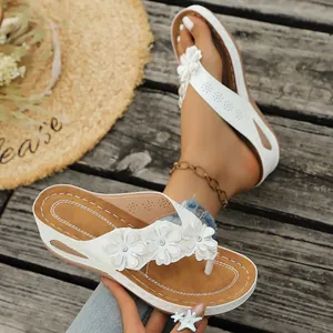 Detalle de las chanclas con cuña blancas para mujer con flores y pedrería fina