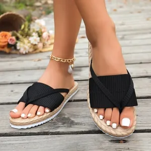 Close-up view of black knit strap flip-flops with straw-textured sole worn on feet outdoors
