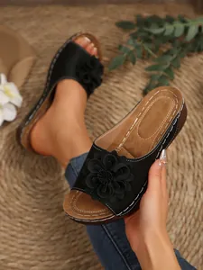 Detailed view of women's black wedge sandals featuring a large 3D floral decoration