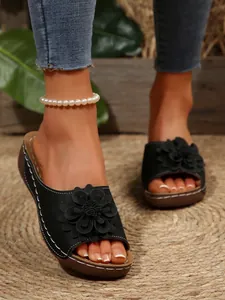 Close-up view of elegant black floral wedge sandals worn on feet against a rustic background