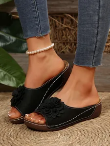 Detailed view of black wedge sandals with a floral accent and pearl anklet detail.