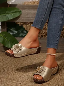 Elegant golden wedge sandals featuring a large floral accent and a comfortable brown platform sole.