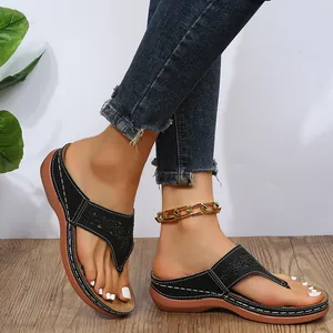 Primer plano de sandalias de cuña negras con patrones calados sobre un suelo de madera