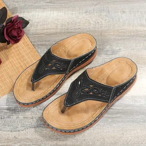 Detalle de chanclas de cuña negras para mujer con calados láser y costuras blancas decorativas.