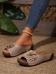 Detail view of beige wedge sandals featuring a large 3D flower and laser-cut patterns