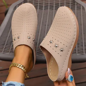 Close-up detail of beige closed-toe platform slippers with floral perforations and studs