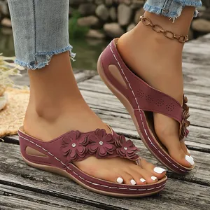 Detalle de sandalias de cuña color burdeos con flores sobre cubierta de madera