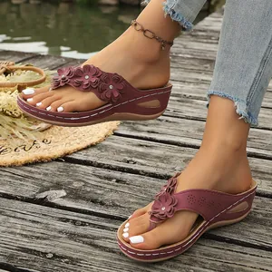 Detalle de sandalias de cuña granates con flores de cuero en una plataforma de madera.