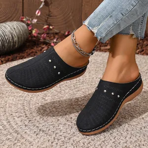 Close-up of black perforated wedge mules with silver stud details on a model