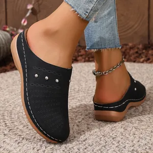Detail view of women's black closed-toe wedge mules with decorative laser-cut patterns