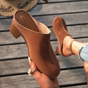 Vue détaillée de mules marron à talons carrés et surpiqûres blanches sur terrasse.