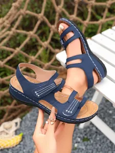 Detailopname van marineblauwe platte Romeinse sandalen met klittenband en witte stiksels