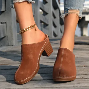 Détail de mules marron à bout fermé avec coutures blanches et talons carrés.