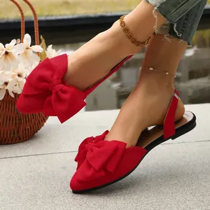 Detailed view of red pointed-toe flat sandals with an oversized bow on model