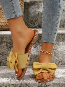 Close-up of yellow flat bow sandals featuring elegant rhinestone edge and textile texture.