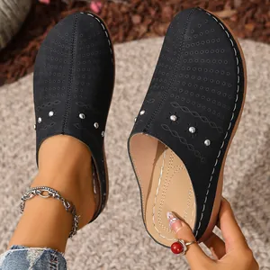 Close-up of black closed-toe platform slippers with laser-cut patterns and studs