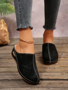 Detailed view of black suede platform mules featuring bold white contrast stitching