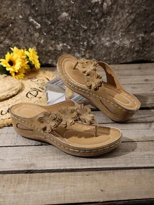 Detailed view of women's wedge flip-flops with elegant floral ornaments on tan straps