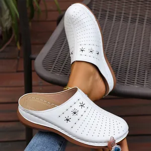 Close-up detail of white perforated wedge clogs with floral rivets and platform sole